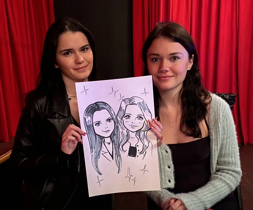 Two friends holding their hand-drawn anime-inspired portraits on paper