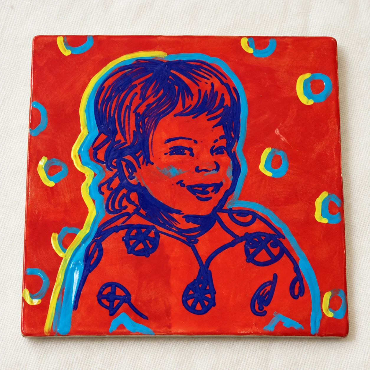 A smiling child painted in pop art style on a red tile